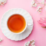 Cup of tea with fresh flowers on pink background. Copy space. Top view